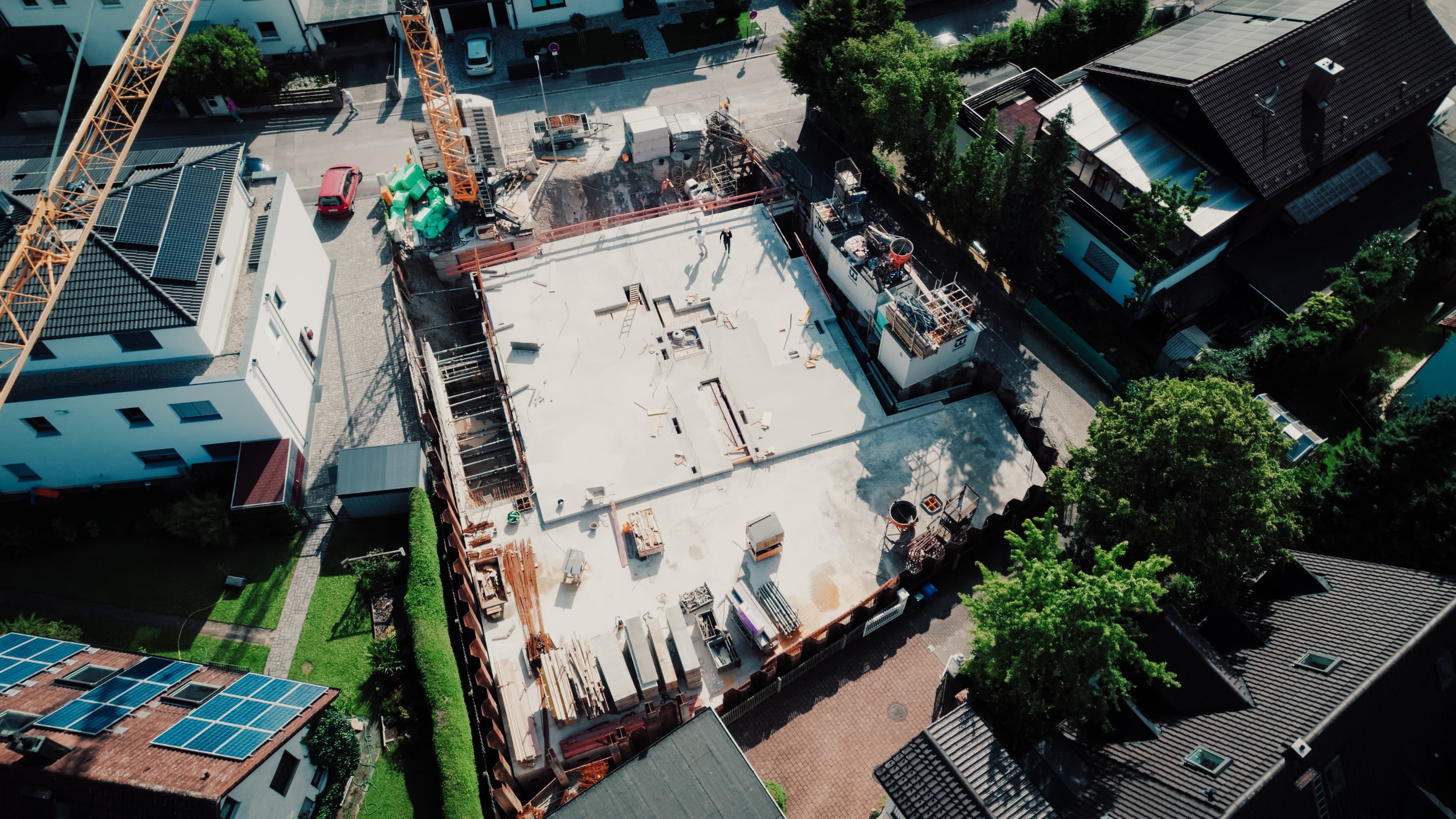 Luftaufnahme einer Baustelle: Rohbau-Decke mit Bewehrungsstahl; zwei Personen mit Bauhelmen besprechen die Arbeiten